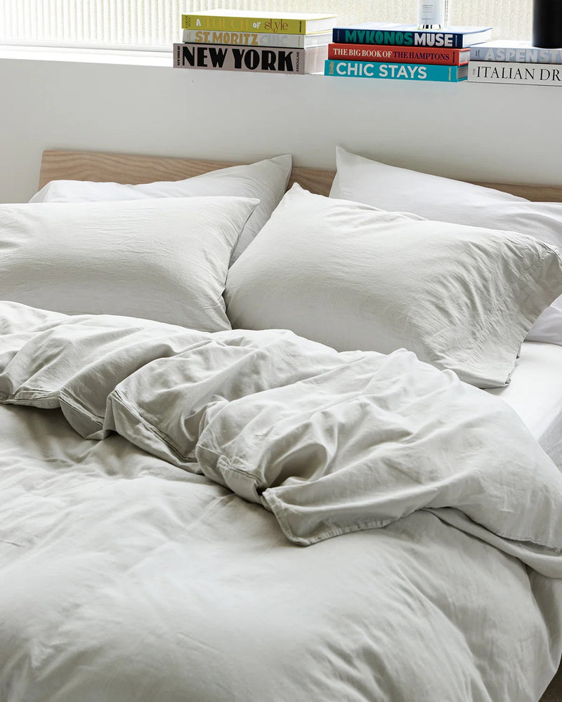 A bedroom with an bed with an off white douvet with 4 large pillows looking like someone hastily made it after getting up in the morning 