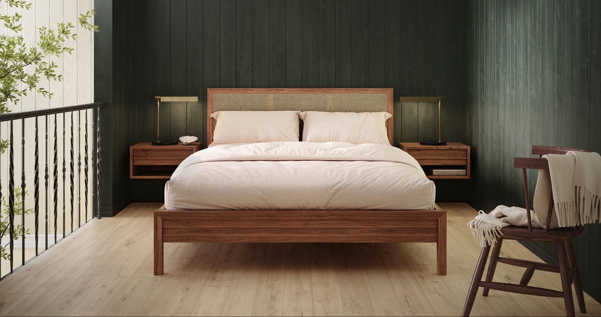 A modern bedroom featuring a wooden platform bed with white bedding, flanked by matching wooden nightstands with lamps, set against a dark green paneled wall and a light wood floor.