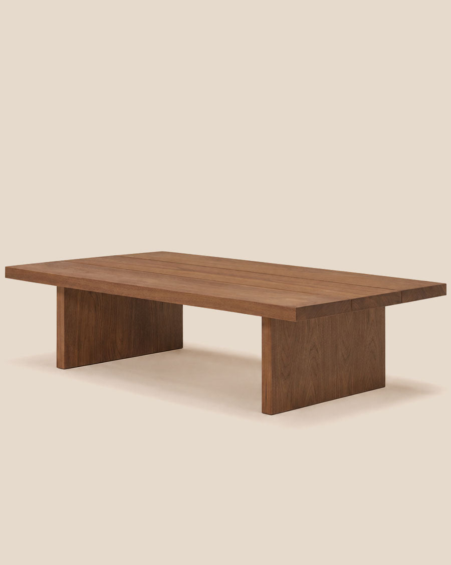 Un gros plan d'une table basse moderne en bois avec une finition en noyer brun foncé, sur fond blanc cassé épuré.